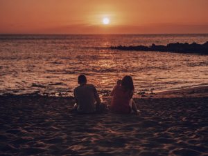 two people sitting on beach at sunset