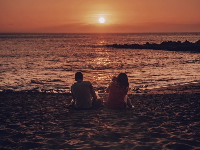 Couple sitting on the beach watching a peaceful sunset over the ocean