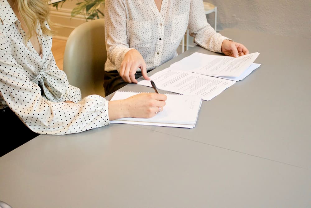 Two women sitting close discussing documents on the table in front of them