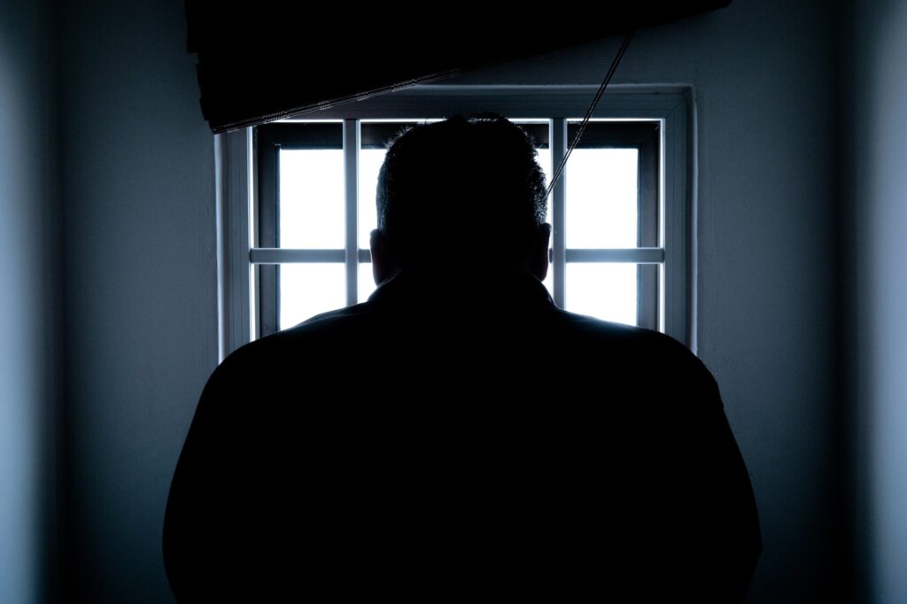 dark image with figure standing behind bars|Man in suit crying